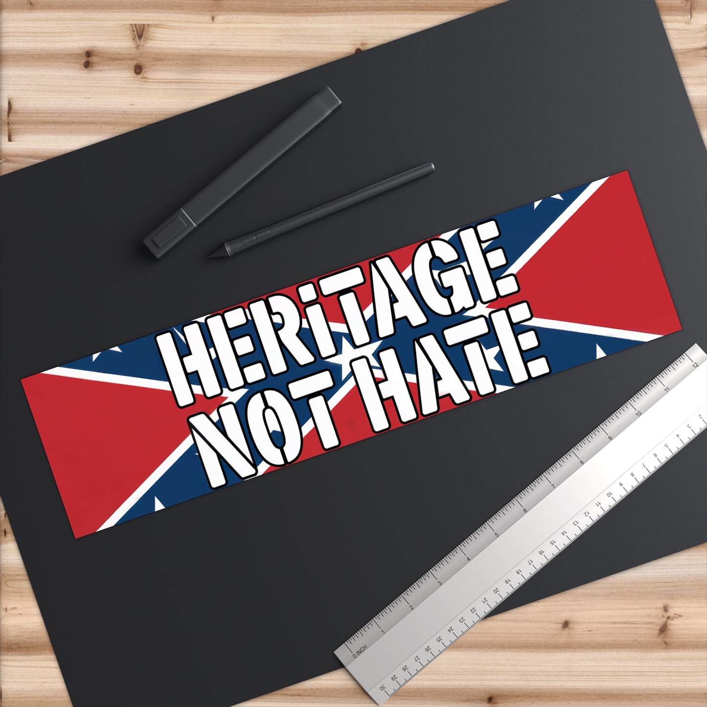 heritage not hate bumper sticker with bold white text on a red and blue background laid on a black desk surface