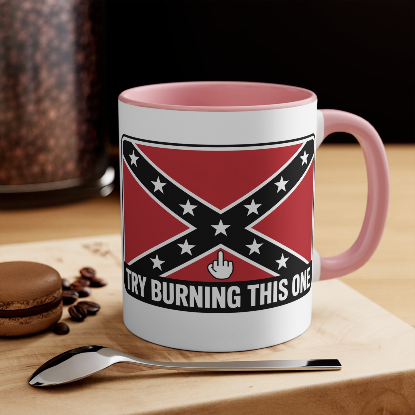 mug with Confederate flag mug design and pink handle on a wooden surface with spoon and macaron
