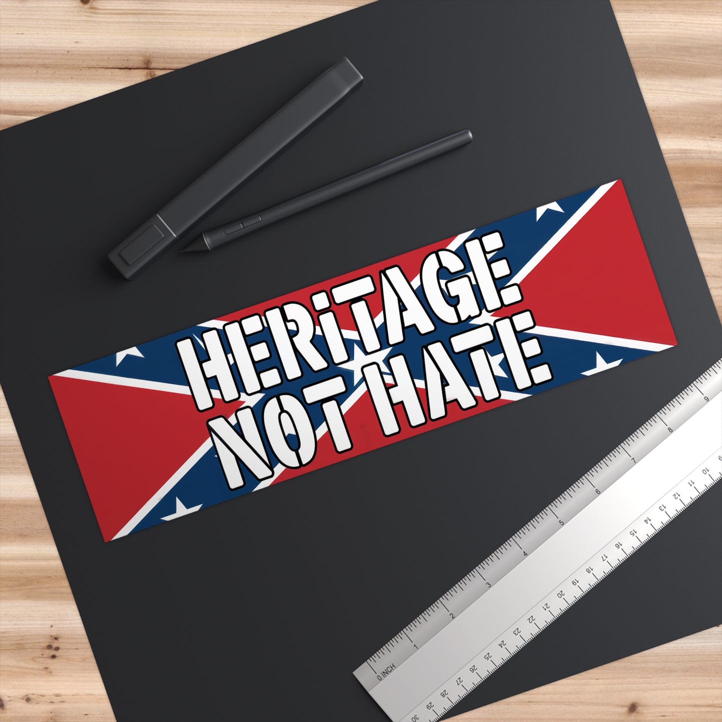 Heritage not hate bumper sticker with Confederate flag design placed on black paper with pen and ruler